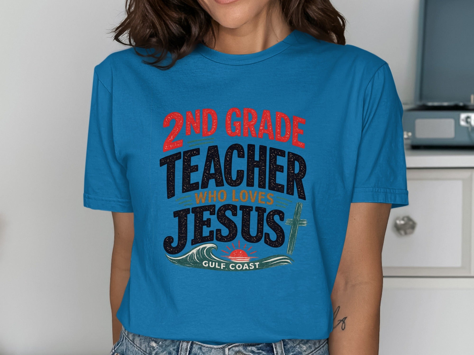Teal t-shirt with "2nd grade teacher who loves Jesus" text and a sun and waves graphic.