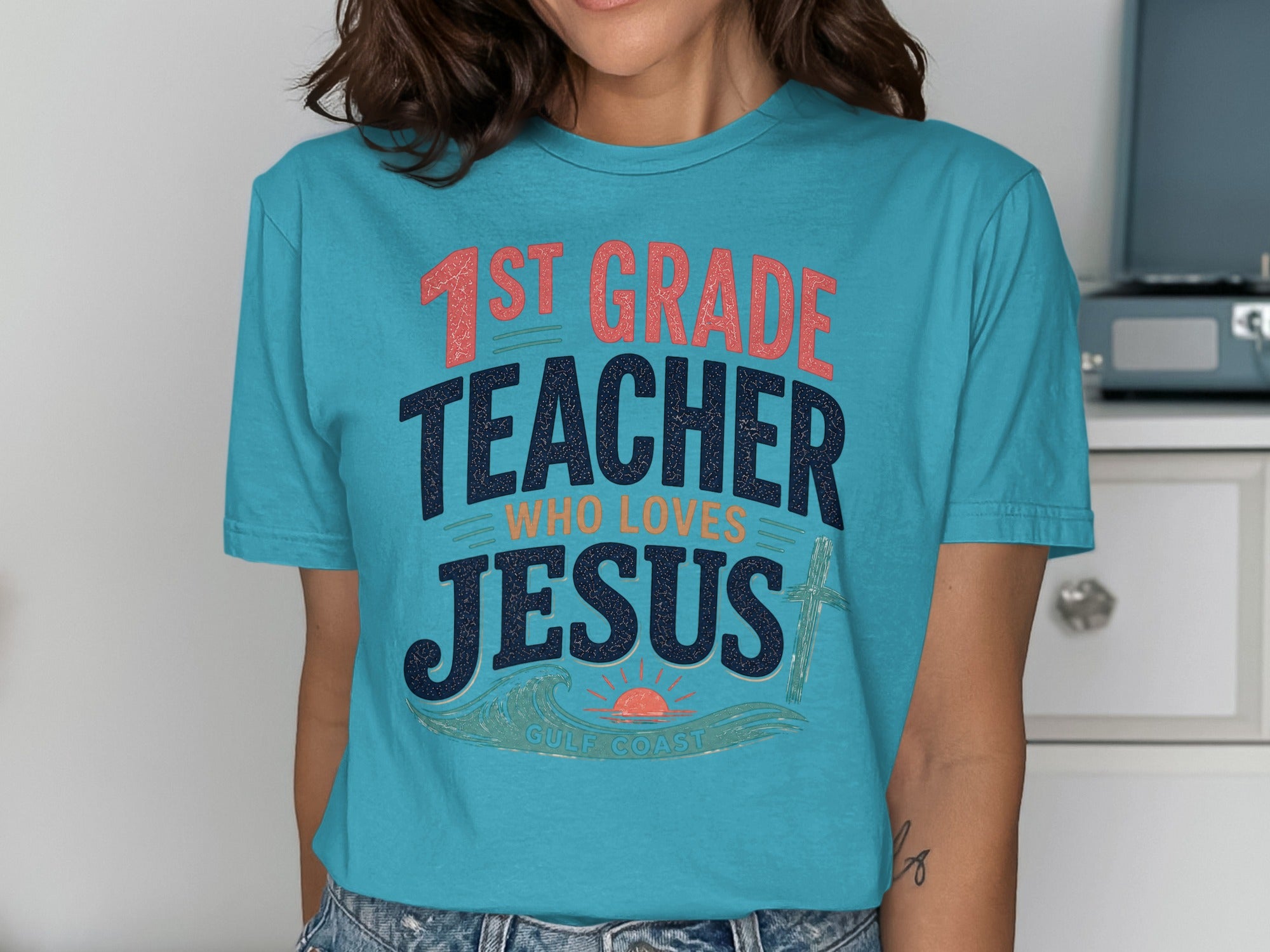 Teal t-shirt with "1st GRADE TEACHER WHO LOVES JESUS" and sun and wave design.