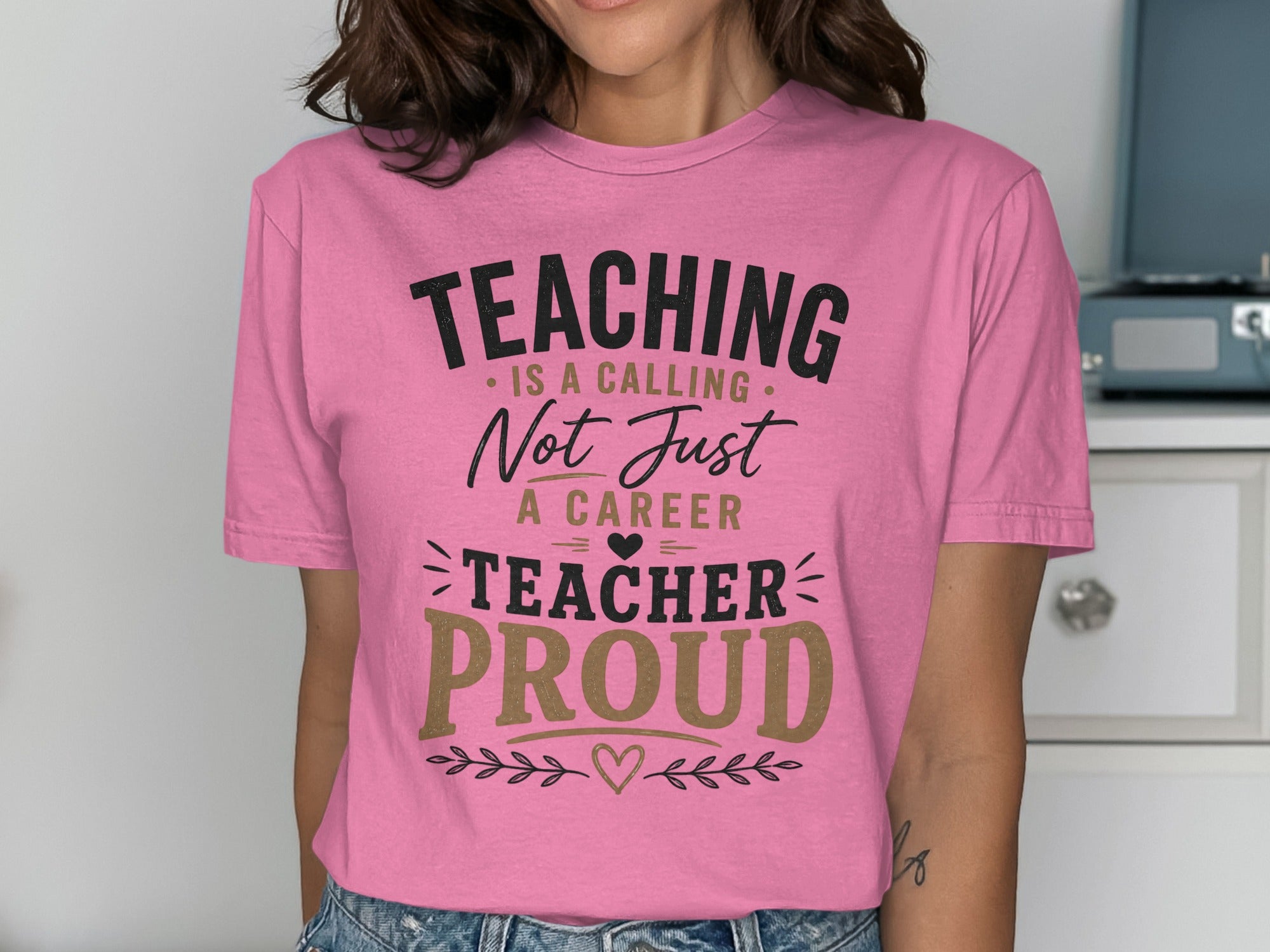 Pink t-shirt with black and gold text reading "TEACHING IS A CALLING NOT JUST A CAREER TEACHER PROUD".