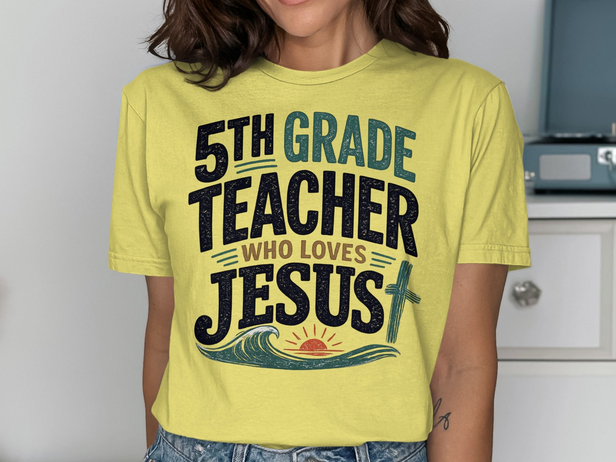 Yellow t-shirt with "5th Grade Teacher Who Loves Jesus" text and wave/sun graphic.