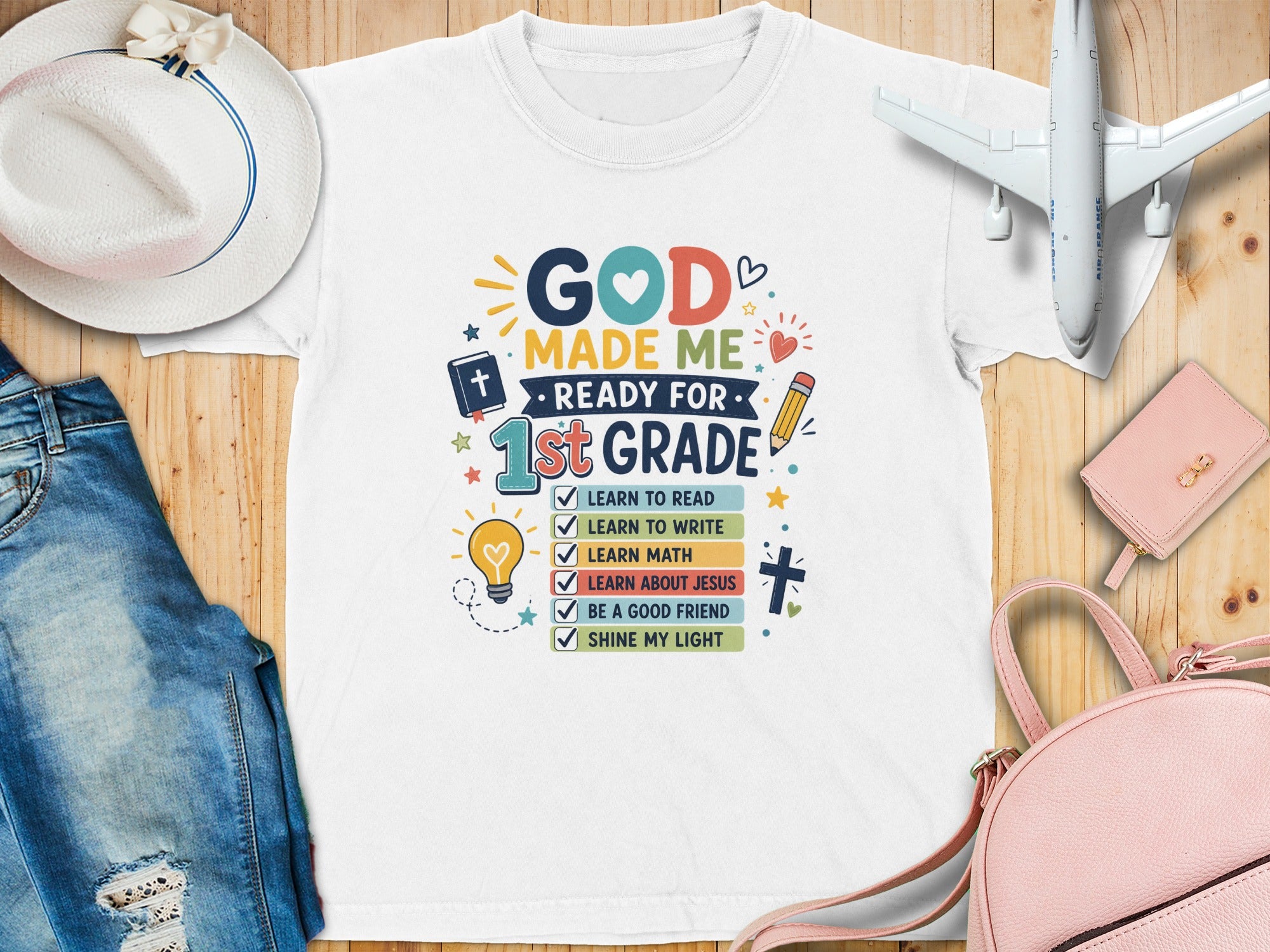 White t-shirt for 1st graders with colorful text and graphics about school and faith.