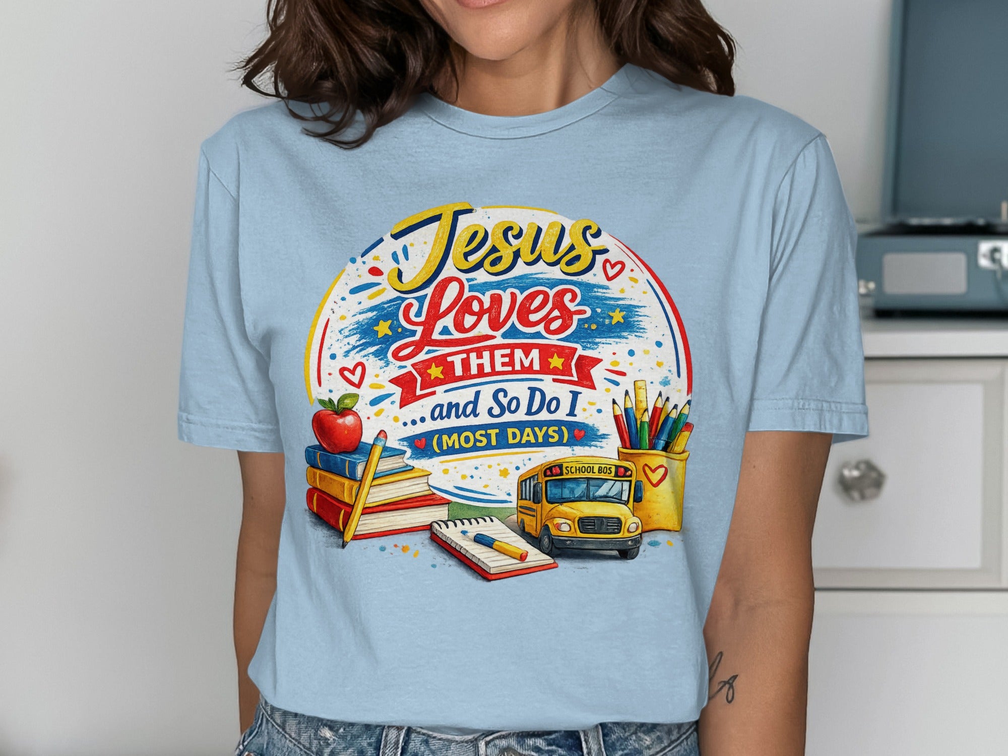 Light blue t-shirt with "Jesus Loves Them... And So Do I" text, school bus, pencils, and apple.