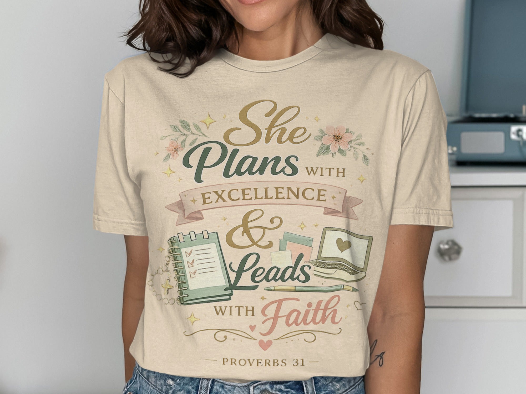 T-shirt with "She Plans with Excellence & Leads with Faith" text and notebook graphic.
