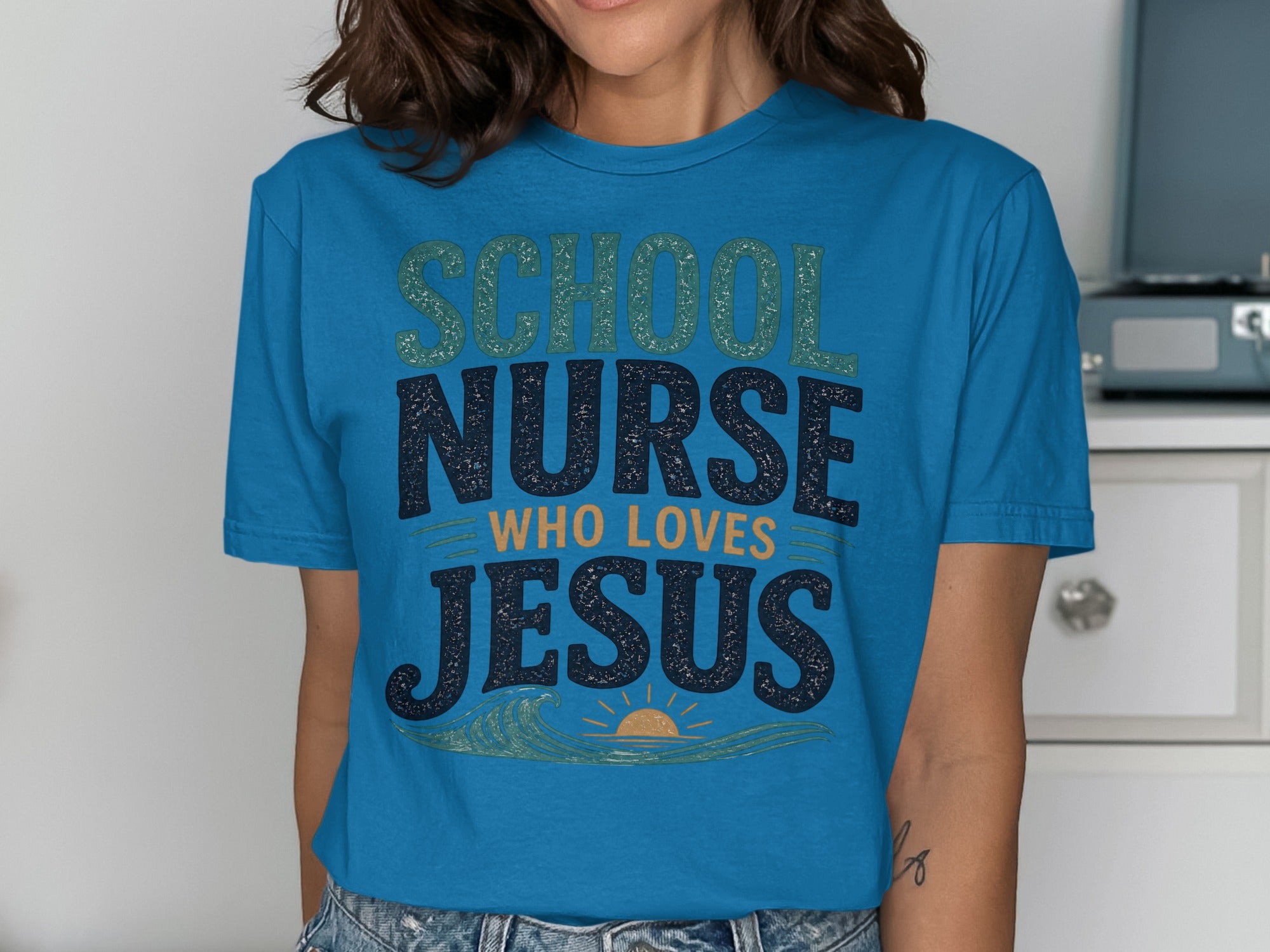 Blue t-shirt with "School Nurse Who Loves Jesus" text and a wavy sun graphic.