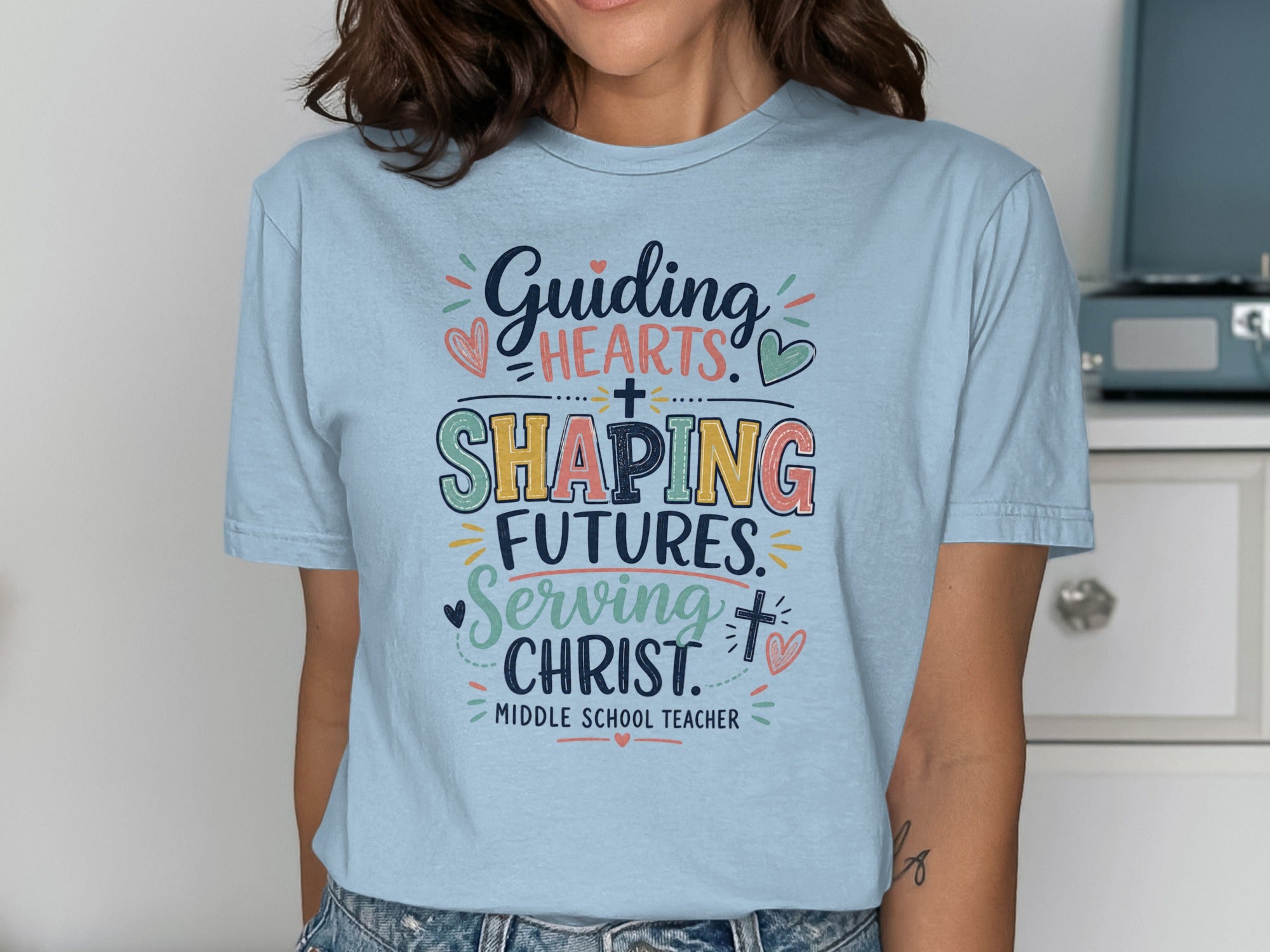 Light blue t-shirt with text "Guiding Hearts, Shaping Futures, Serving Christ. Middle School Teacher".