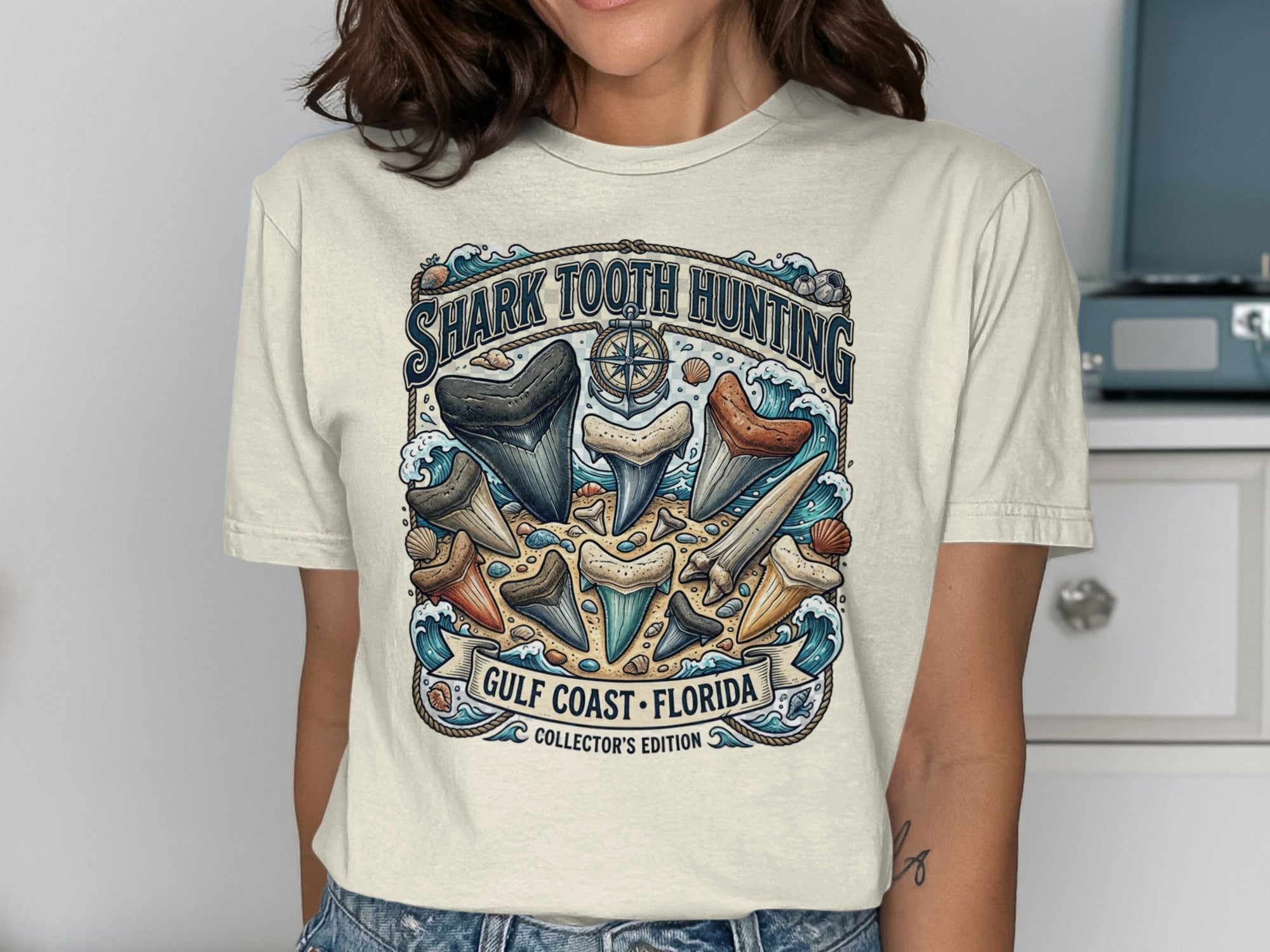 T-shirt graphic with shark teeth, waves, and text "SHARK TOOTH HUNTING GULF COAST FLORIDA COLLECTOR'S EDITION".