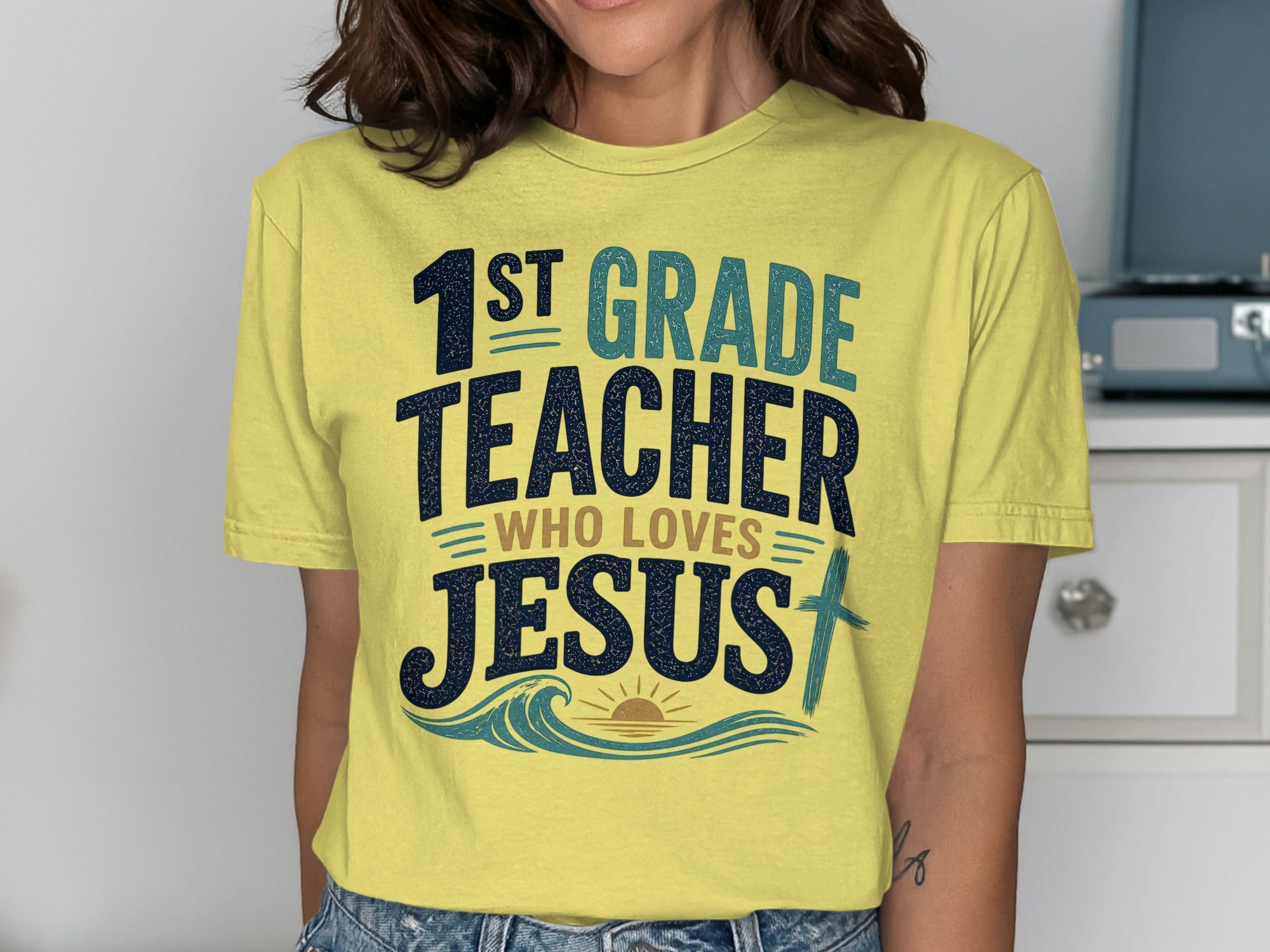 Yellow t-shirt with "1st grade teacher who loves Jesus" text and a cross.