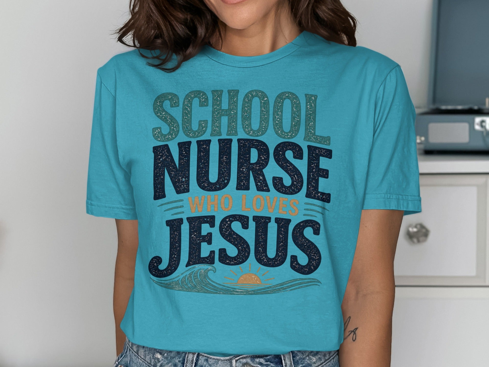 Teal t-shirt with "School Nurse Who Loves Jesus" text and a wavy sun graphic.
