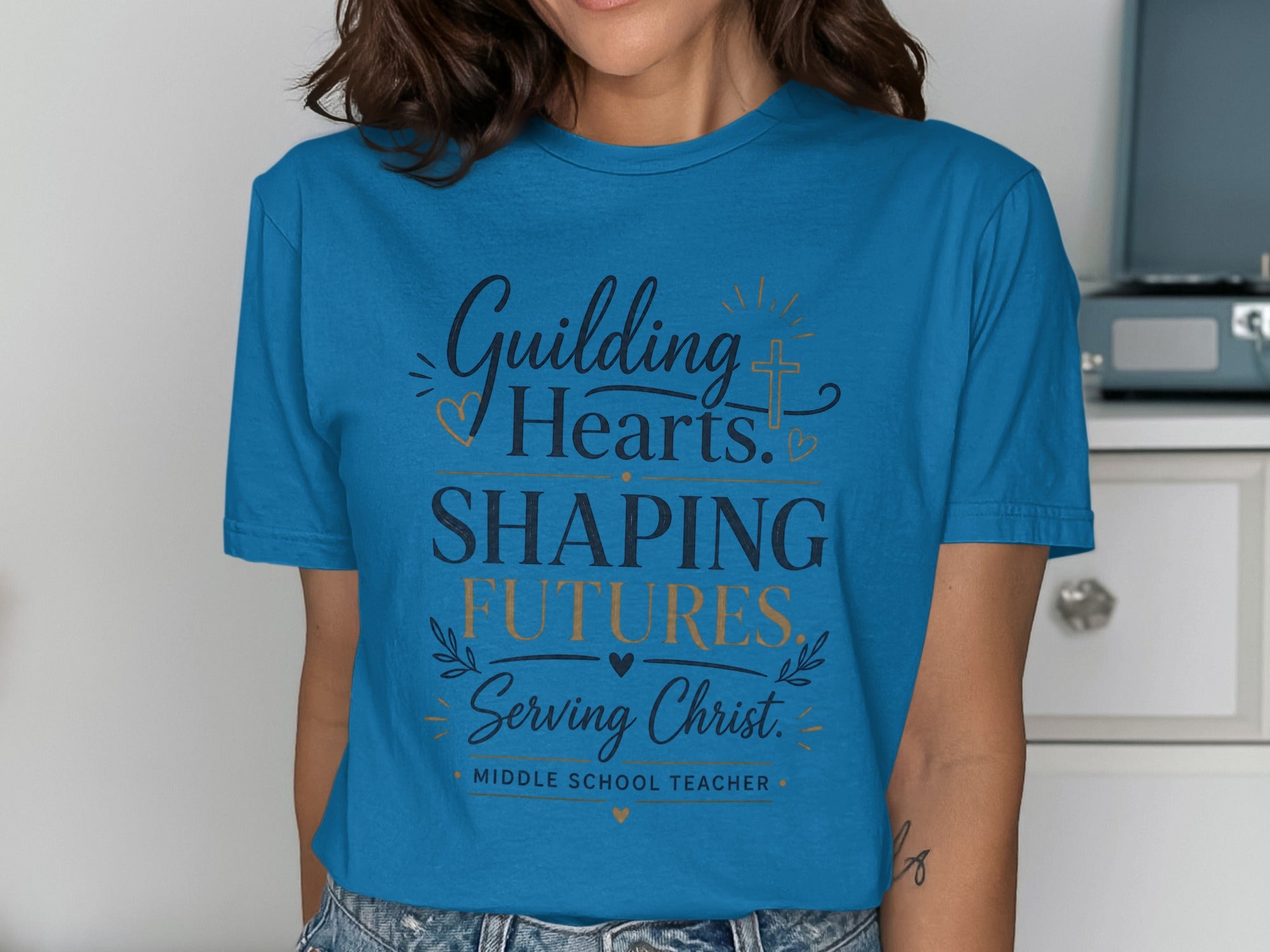 Teal t-shirt with "Guiding Hearts Shaping Futures Serving Christ" text.
