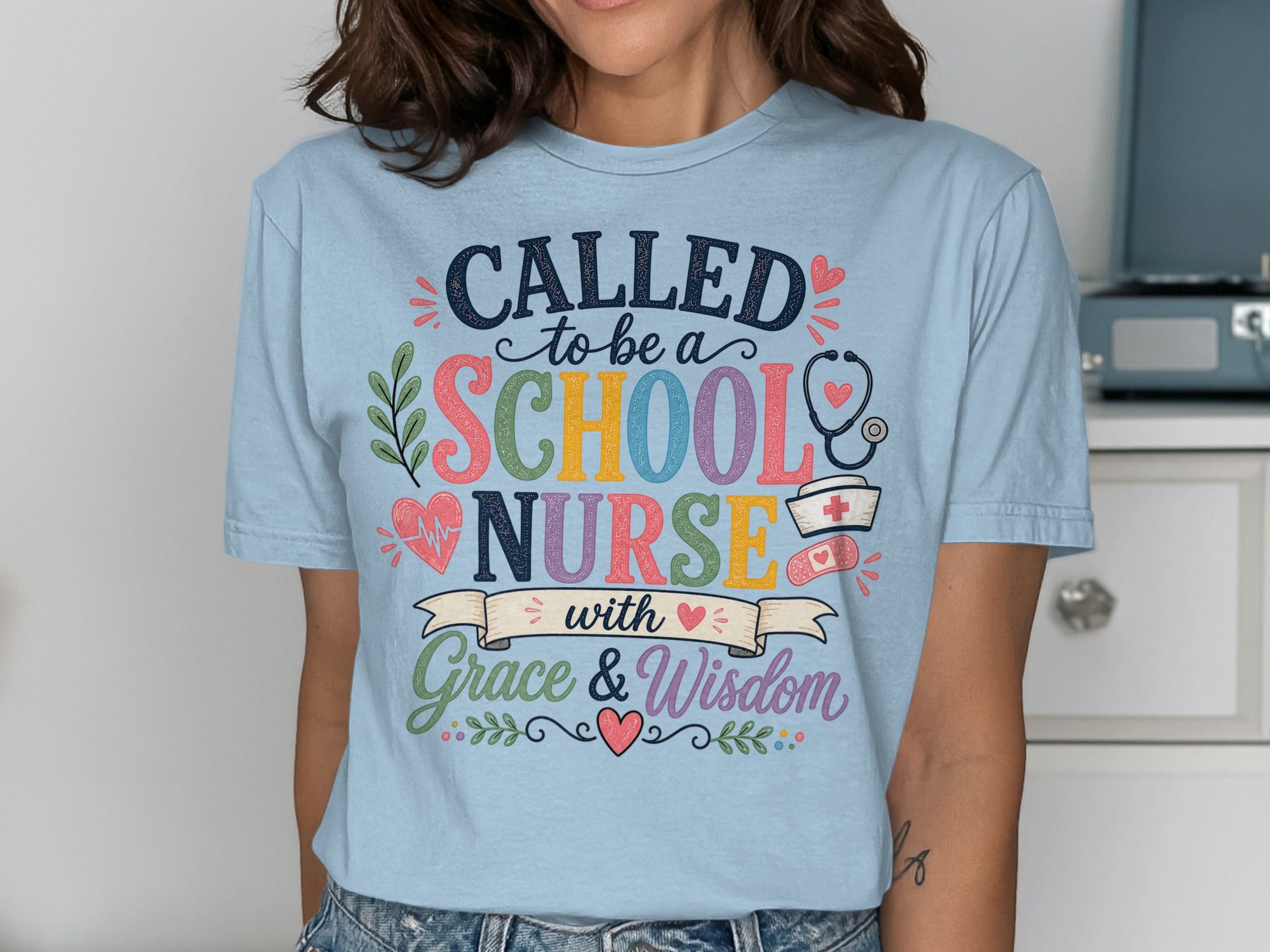 Light blue t-shirt with "Called to be a School Nurse with Grace & Wisdom" text and medical icons.