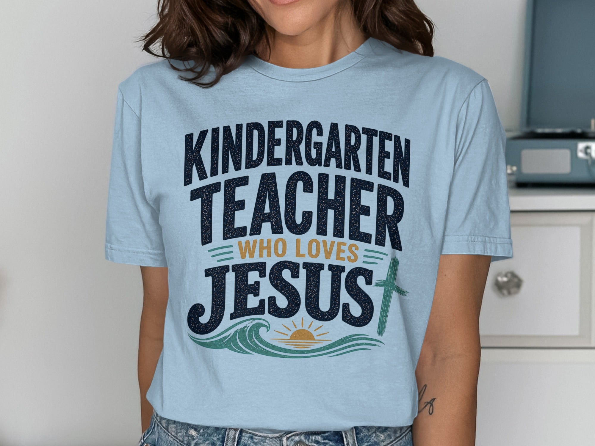 Light blue t-shirt with "Kindergarten Teacher Who Loves Jesus" text and cross design.