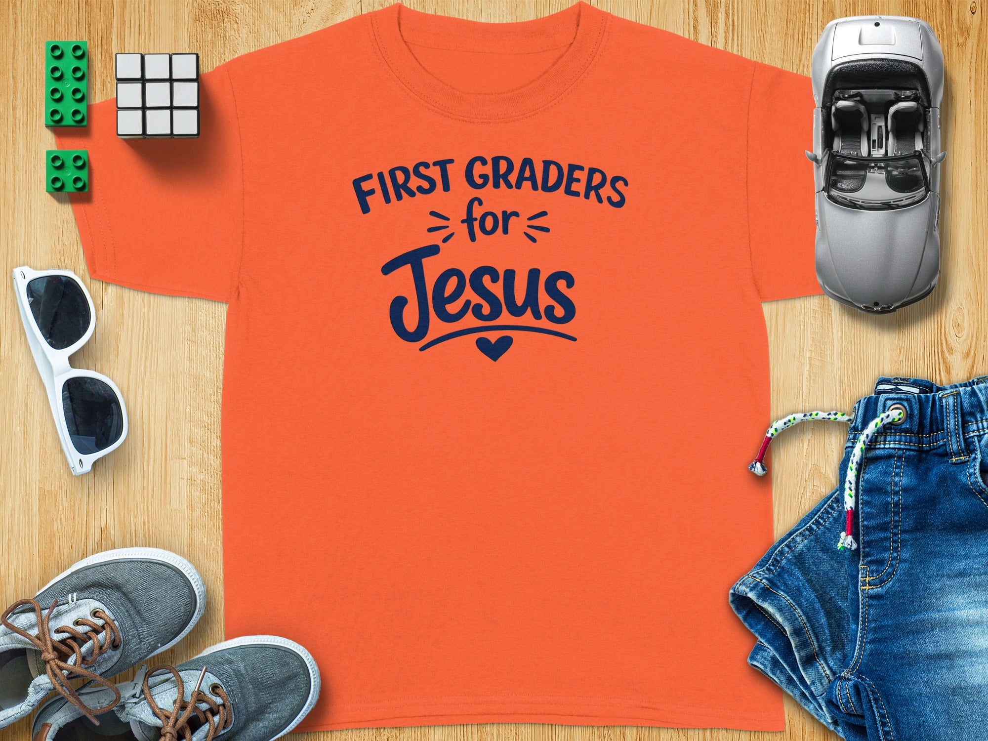 Orange t-shirt with "First Graders for Jesus" text, surrounded by school supplies.