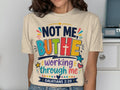Cream t-shirt with colorful "NOT ME, BUT HE" text and Bible verse.