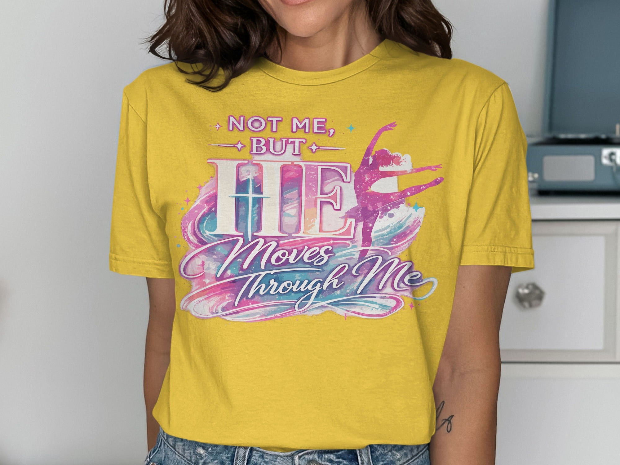 Yellow t-shirt with "Not Me, But He Moves Through Me" and ballerina graphic.