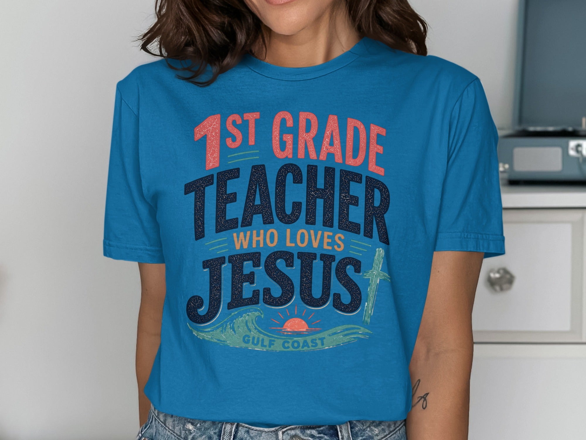 Blue t-shirt with "1st GRADE TEACHER WHO LOVES JESUS" text and ocean waves.