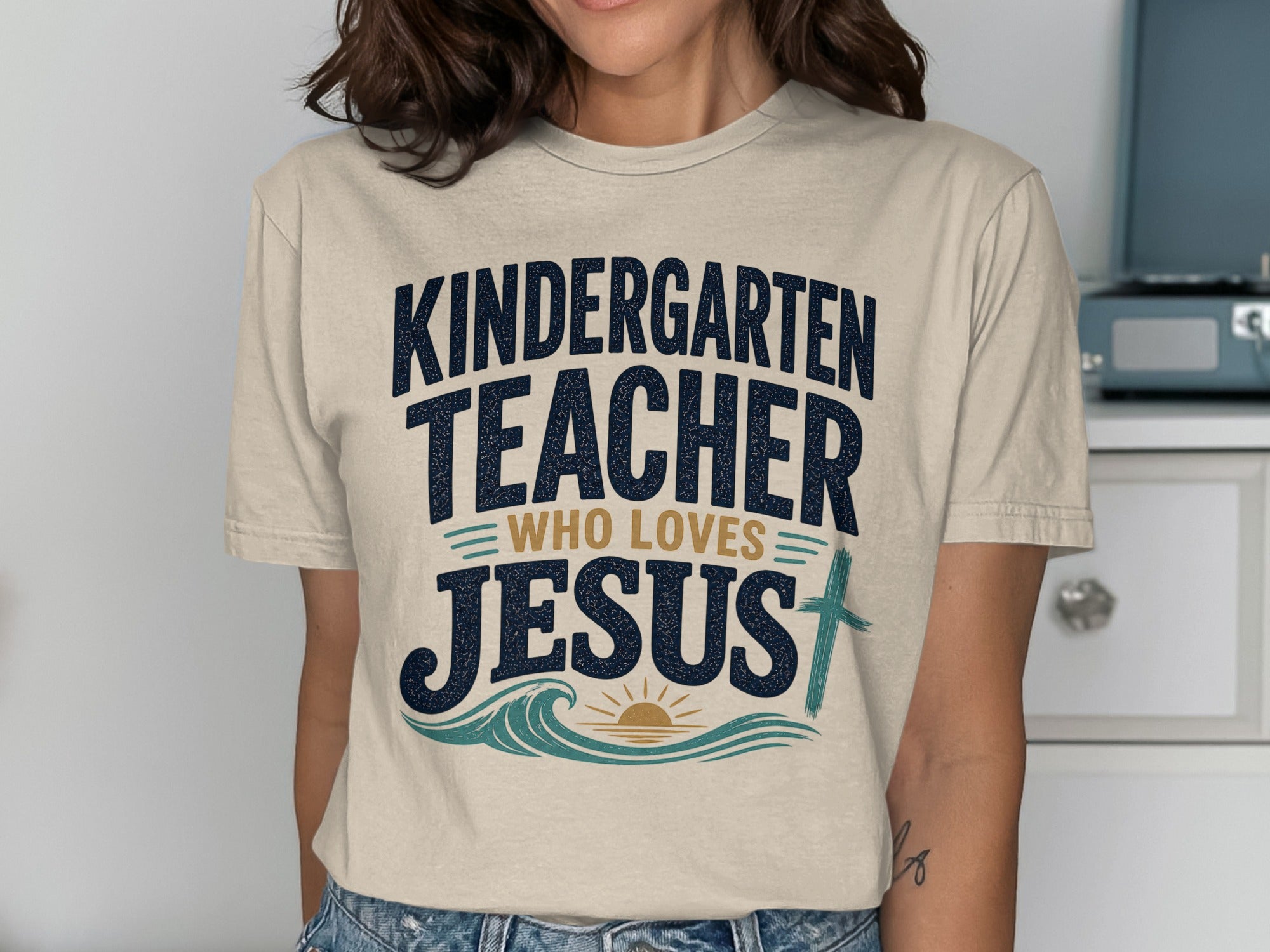 Kindergarten teacher who loves Jesus text with cross, waves, and sun graphic.