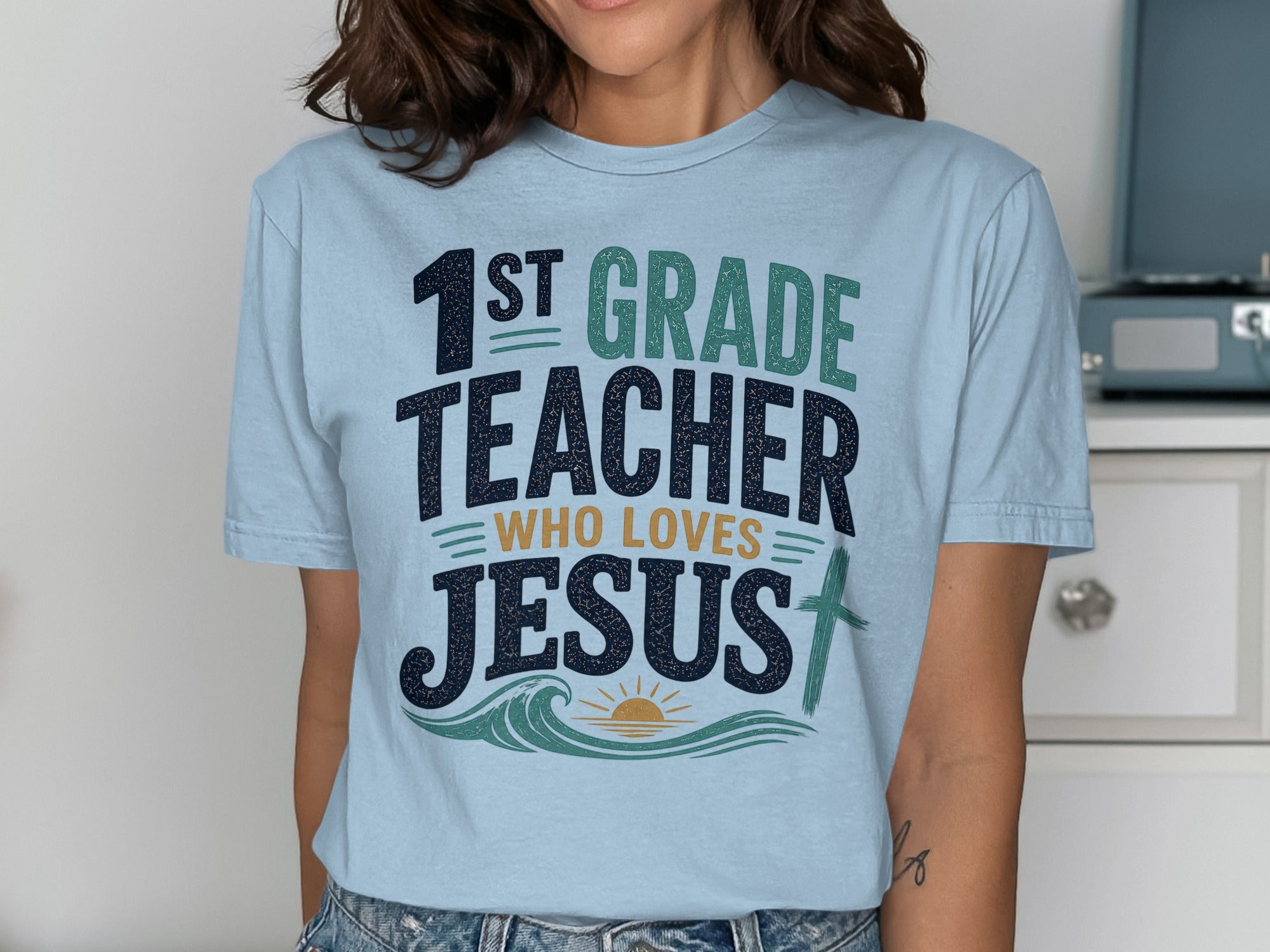 "1st Grade Teacher Who Loves Jesus" graphic tee with waves and a cross.