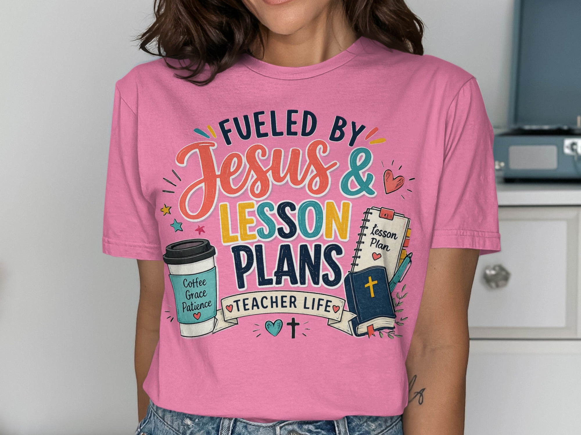 Pink t-shirt with "Fueled by Jesus & Lesson Plans Teacher Life" text and illustrations.