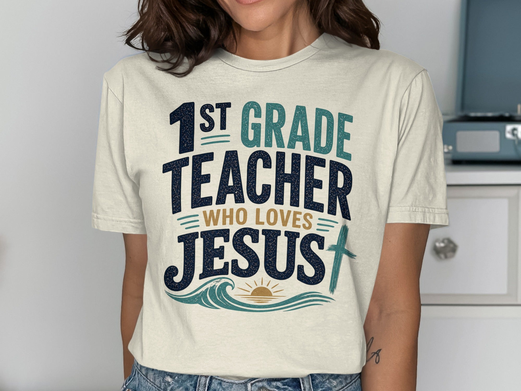 "1st Grade Teacher Who Loves Jesus" graphic t-shirt with wavy design and cross.
