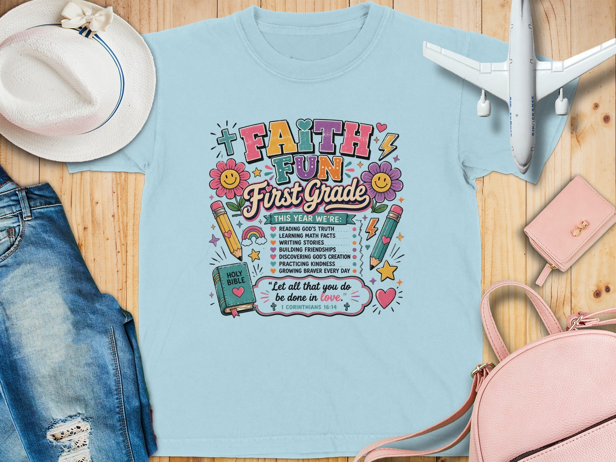 Light blue t-shirt with "Faith & Fun First Grade" graphic, Bible verses, and school-related icons.