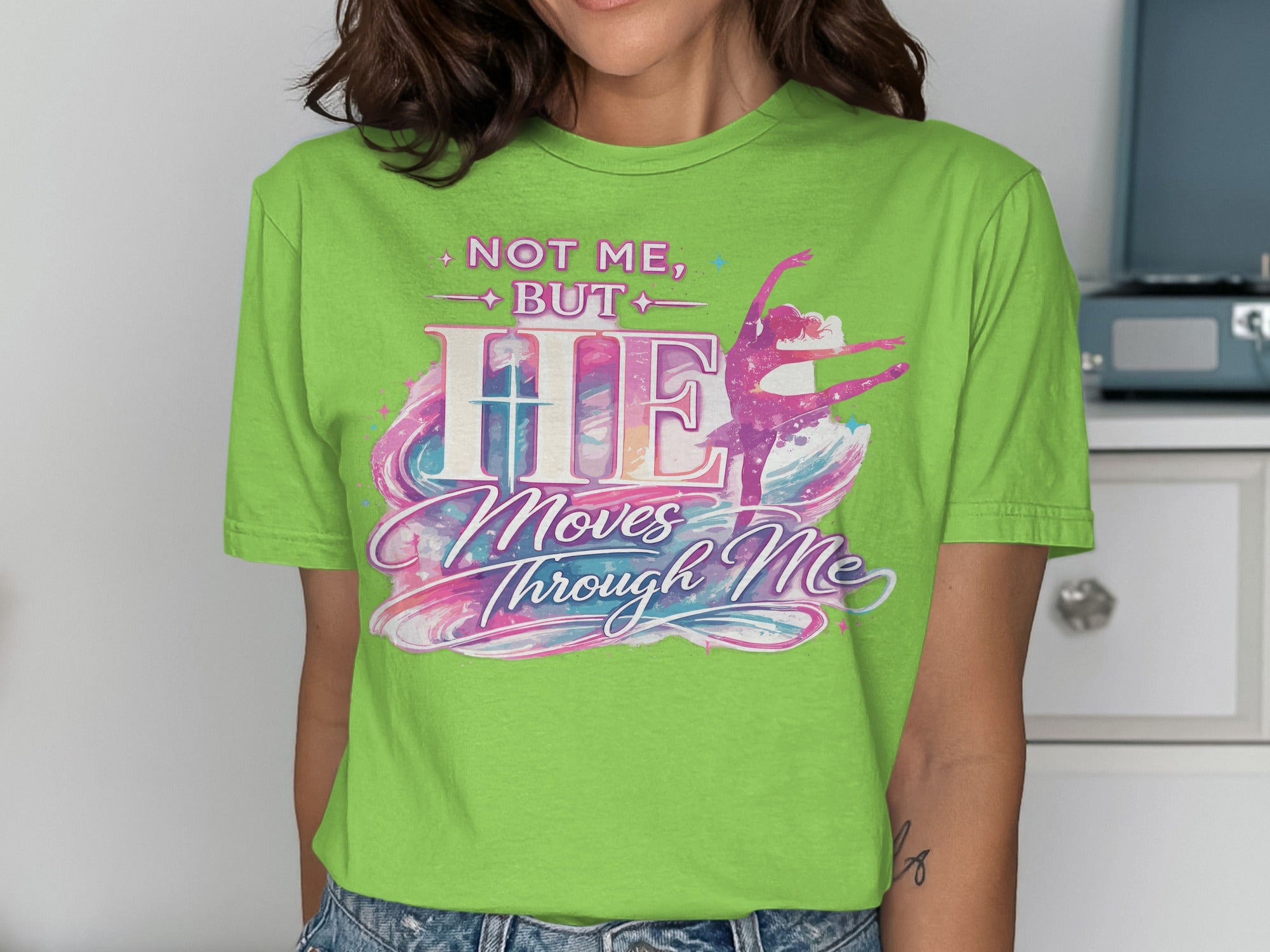 Green t-shirt with pink, purple, and blue "NOT ME, BUT HE Moves Through Me" text and a dancer graphic.