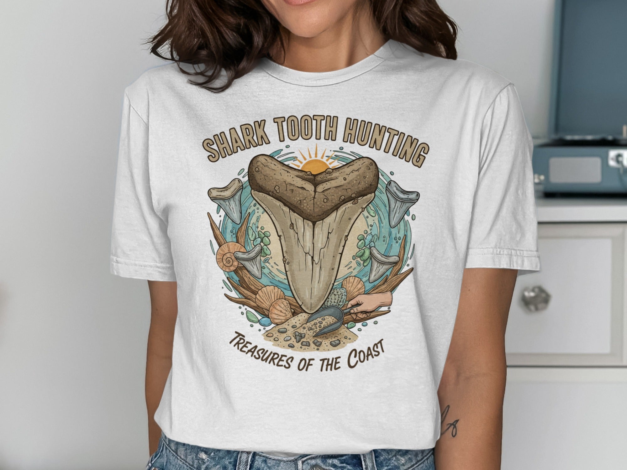 White t-shirt graphic with sharks teeth, shells, and "Shark Tooth Hunting" text.