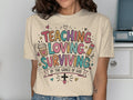T-shirt with "Teaching, Loving, Surviving by the Grace of God" text and playful graphics.