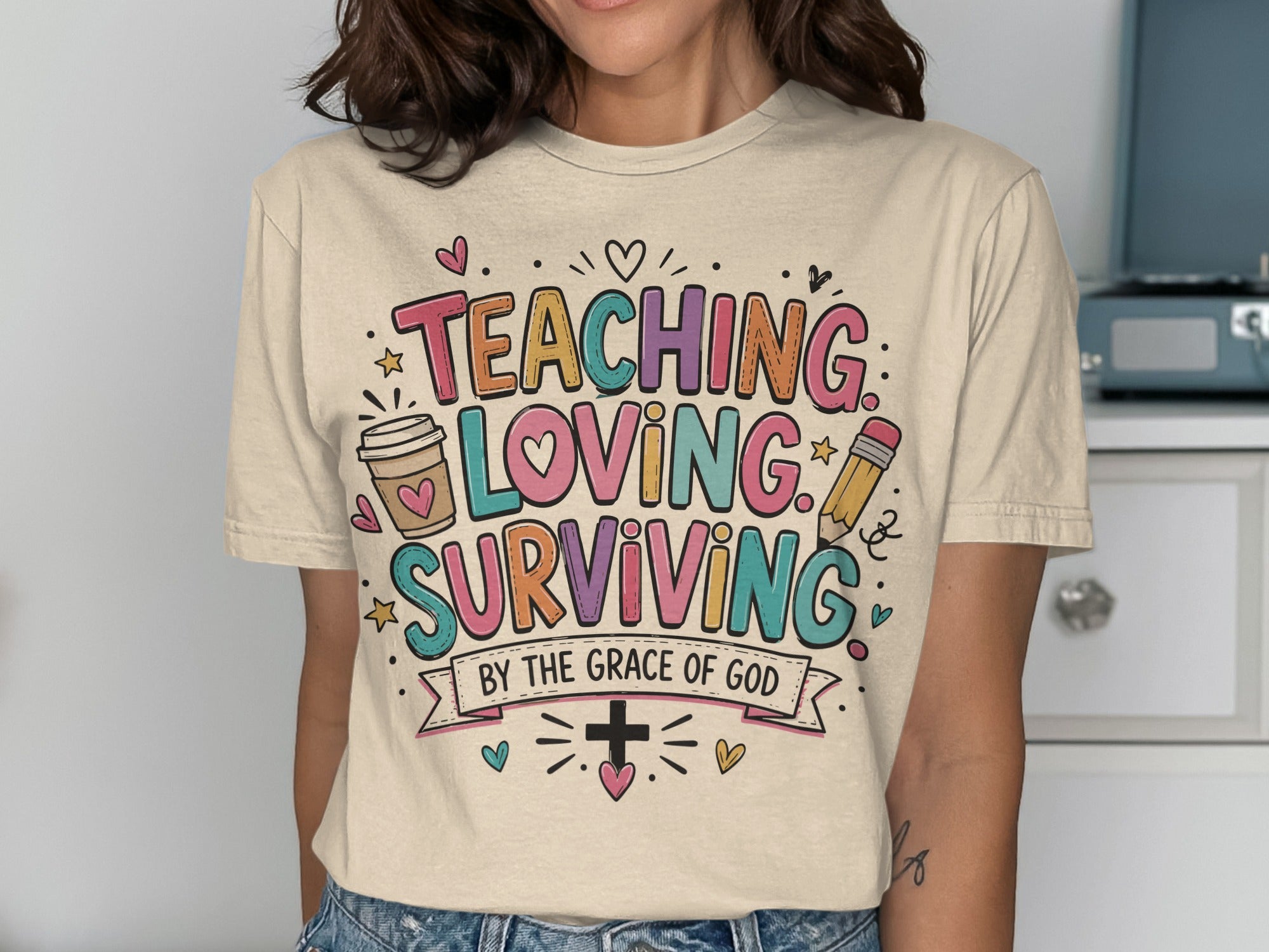 T-shirt with "Teaching, Loving, Surviving by the Grace of God" text and playful graphics.