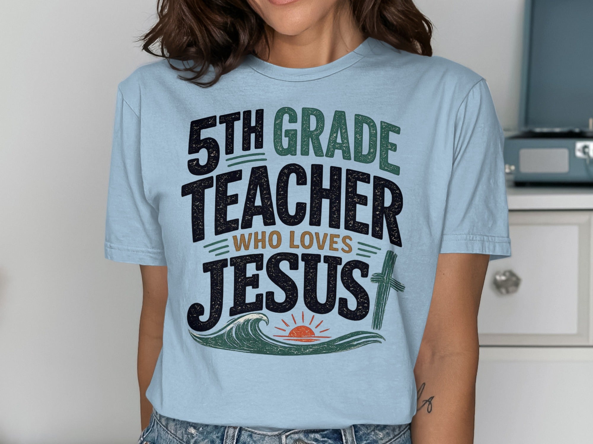 Light blue t-shirt with "5th Grade Teacher Who Loves Jesus" and cross graphic.