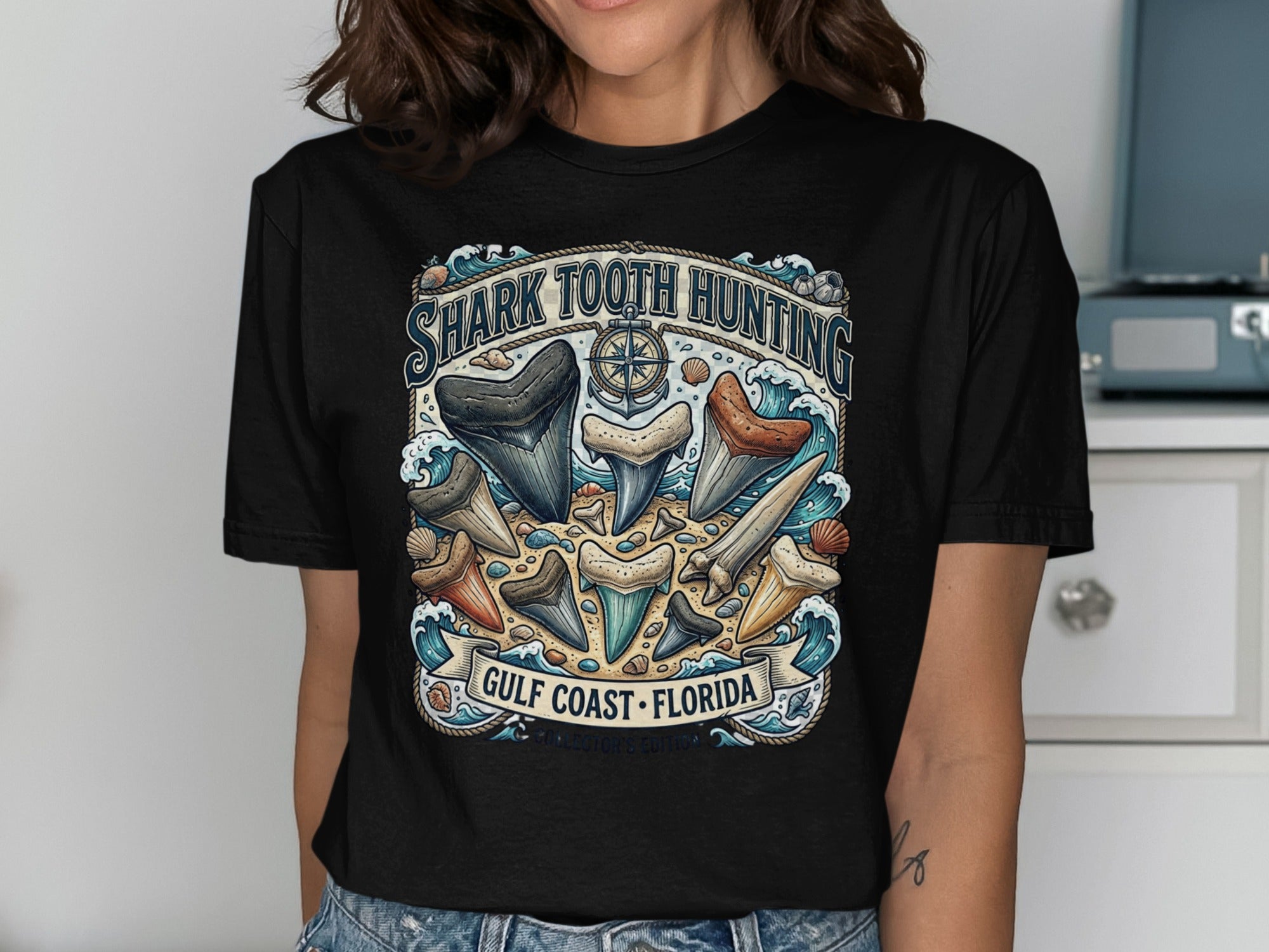 Black t-shirt graphic with various shark teeth and text reading "Shark Tooth Hunting Gulf Coast Florida".