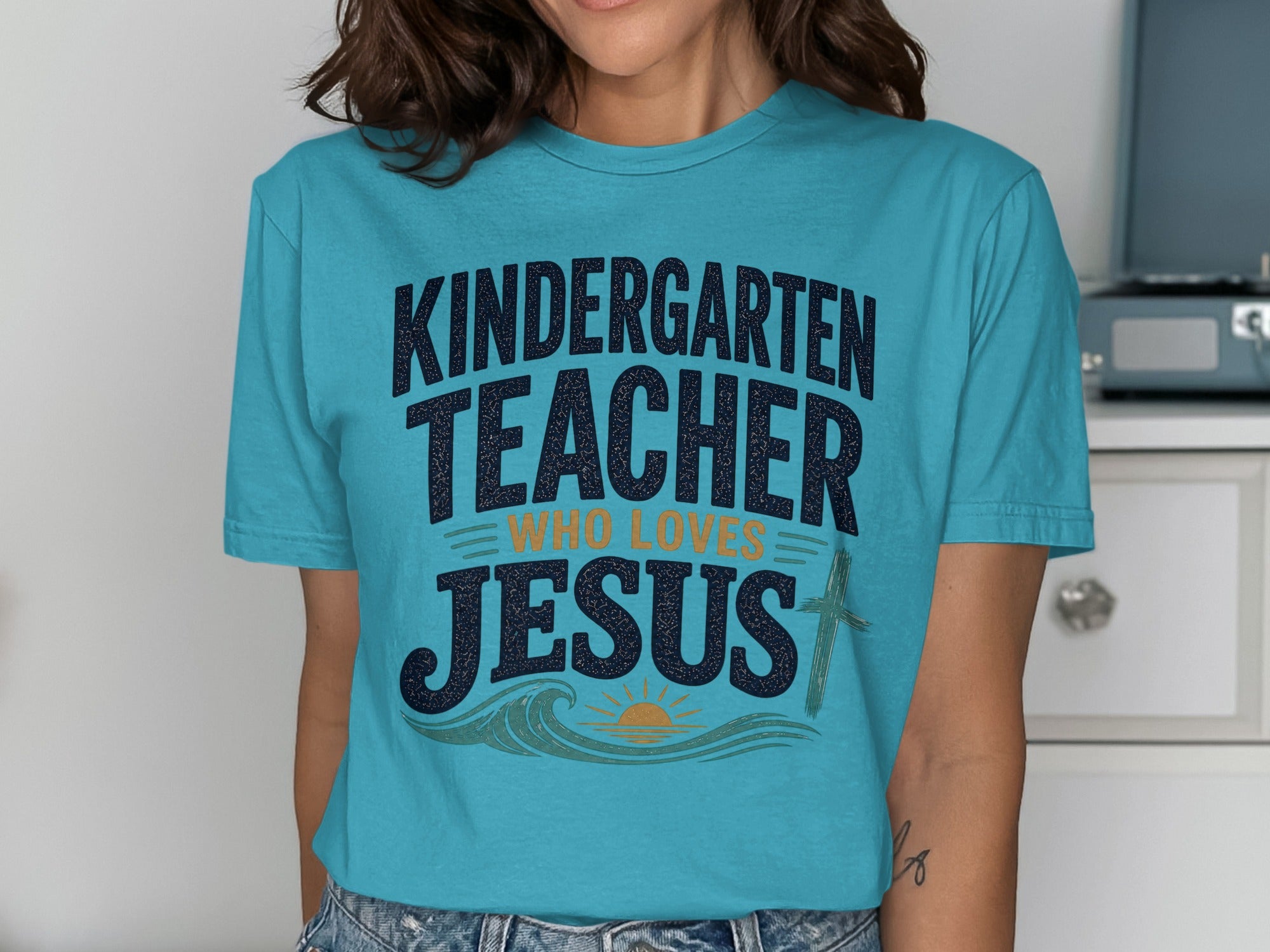 Teal t-shirt with "Kindergarten Teacher Who Loves Jesus" text and wave graphic.